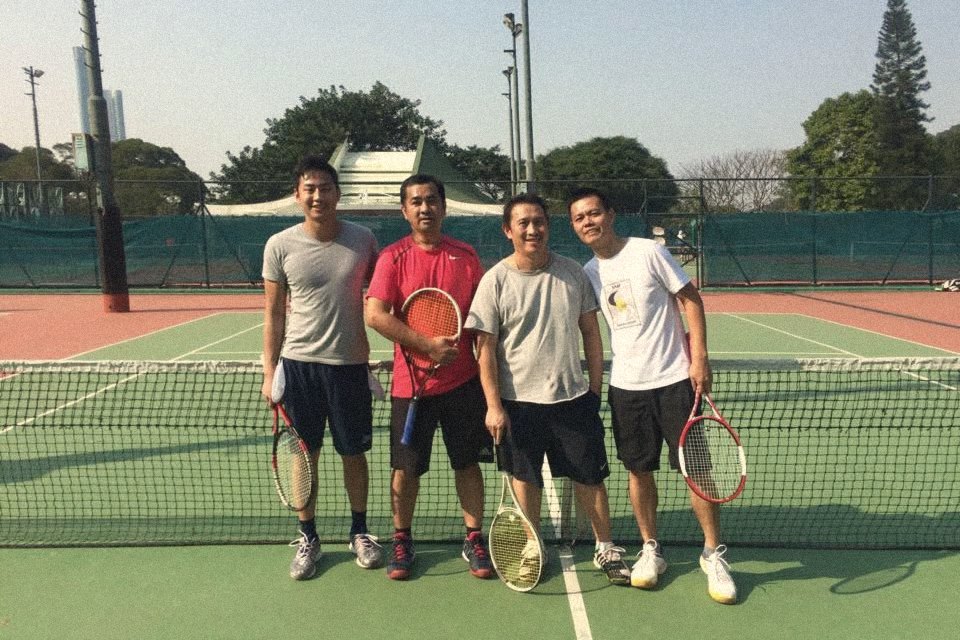 Four players lined up at the net on a sunny outdoor court in Hong Kong, rackets in hand