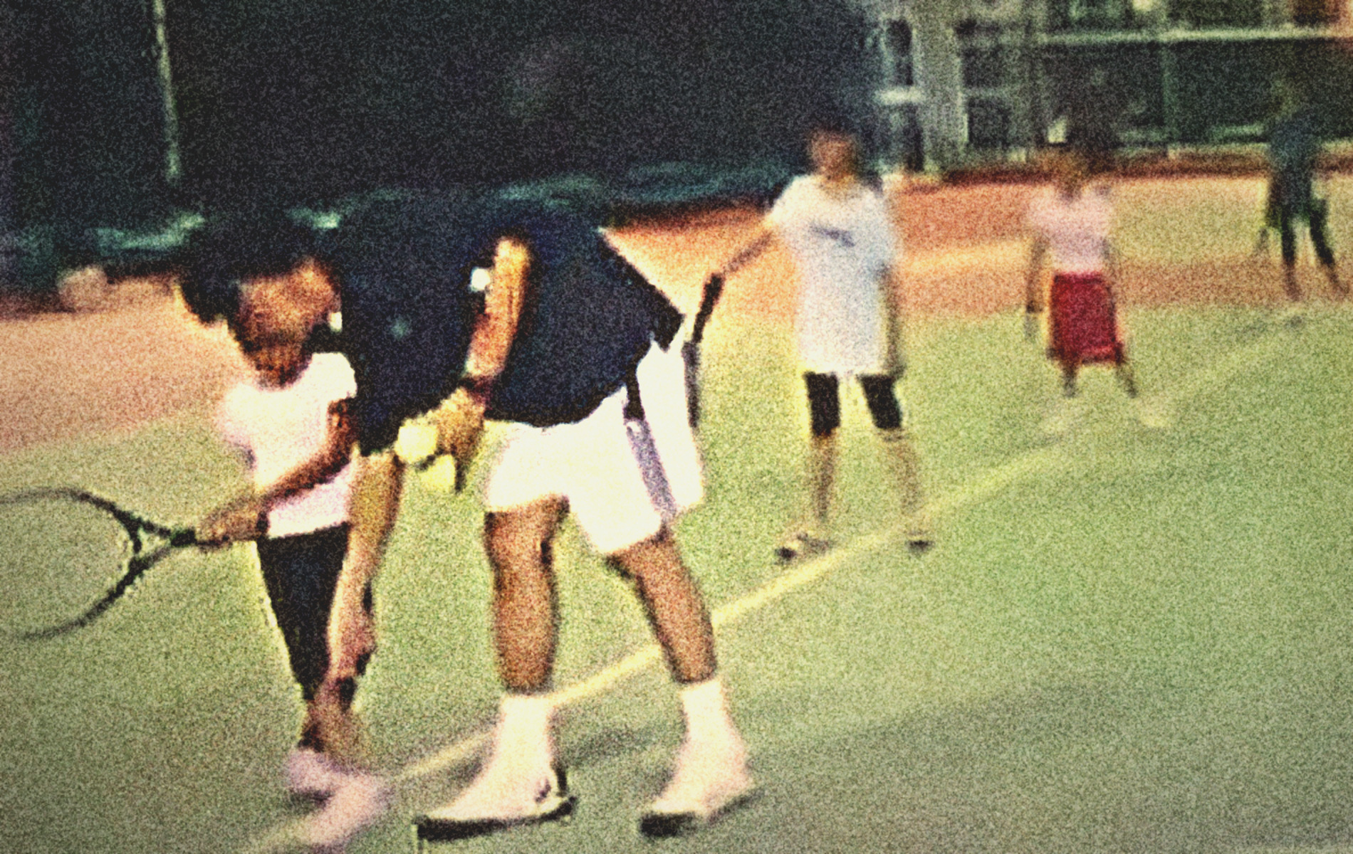 Jaime Gatpandan coaching his daughters on a green court at night; a daughter in a pink shirt swings beside him
