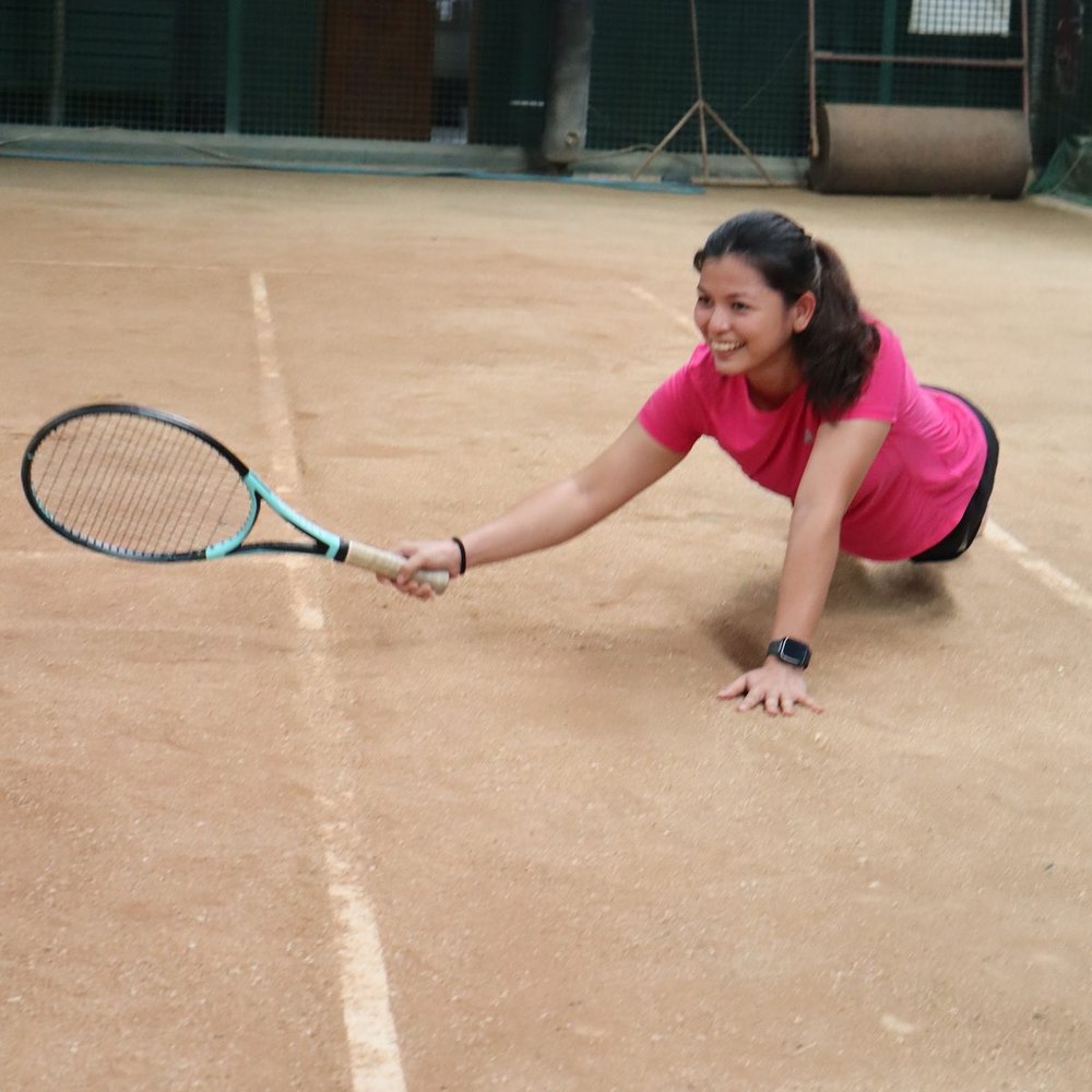 Rally Session 01: player smiling mid-dive for a wide forehand on the indoor clay court