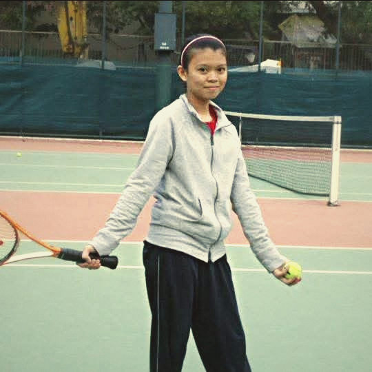 Jade as a girl on court, holding a racket and a ball