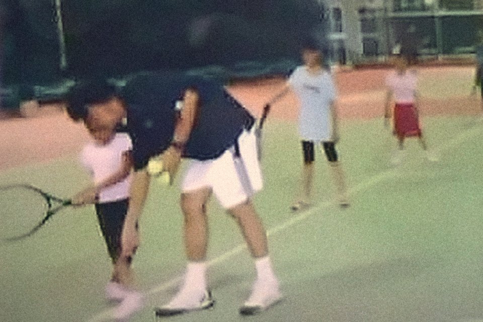 Training session: the coach bent to a young player, showing her the forehand, other juniors waiting behind