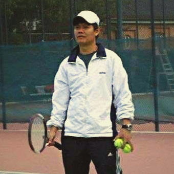 Jaime Gatpandan on court in a white track jacket, holding rackets and tennis balls