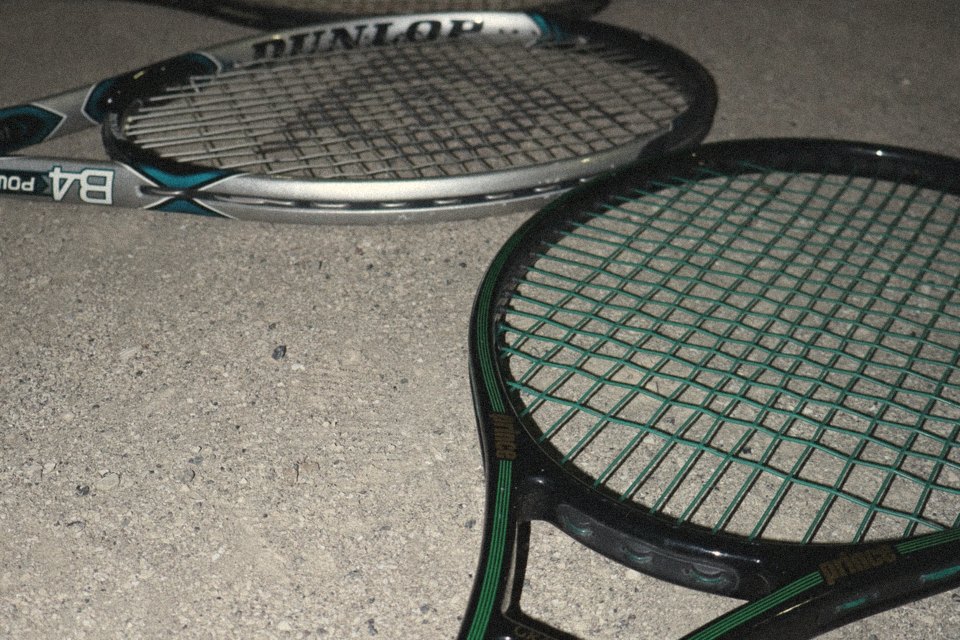 Old rackets laid out on a concrete court at night: a Prince Graphite Oversize in front, a Dunlop behind